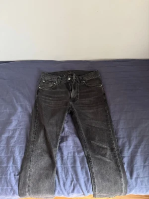 Svarta jeans med fem fickor från Nudie - Snygga svarta jeans med klassisk femficksdesign. Jeansen har en diskret tvättad look och silverfärgade nitar. Passar perfekt till en avslappnad stil och är lätta att matcha med olika plagg. Materialet är denim i bomull.