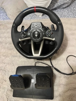 Ratt och pedaler till Xbox - Säljer en svart racingratt med pedaler för Xbox. Ratten har flera knappar, paddlar och en greppvänlig yta i plast och gummi. Pedalenheten har två pedaler och ansluts med kabel. Perfekt för bilspel och racingupplevelser hemma.