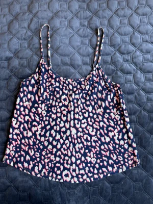 Leopardmönstrad linnetopp i blått och rosa - Säljer en snygg linnetopp med leopardmönster i blått, vitt och rosa. Toppen har tunna axelband och är tillverkad i ett mjukt och lätt material, perfekt för varma dagar. Passar dig som vill sticka ut med ett trendigt mönster.