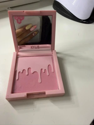 Kylie Cosmetics rosa puderrouge - Säljer ett puderrouge från Kylie Cosmetics i en ljusrosa nyans. Rouget kommer i en fyrkantig rosa dosa med spegel och har det ikoniska dropp-mönstret i pudret. Perfekt för att ge kinderna en fräsch och naturlig look.