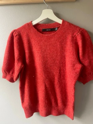 Röd stickad tröja från Vero Moda - Snygg röd stickad tröja från Vero Moda med puffärmar och rund halsringning. Tröjan har korta ärmar och ribbade muddar vid ärmslut och nederkant. Perfekt för dig som vill ha en trendig och mysig look.