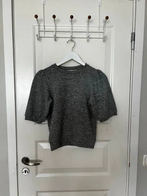 Grå puffärm tröja från lager 157 - Snygg grå tröja från lager 157 med puffade ärmar och rund halsringning. Materialet är mjukt och stickat, perfekt för att skapa en trendig look. Passar dig som gillar stilrena och moderna plagg med en twist.