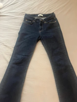 Mörkblå bootcut jeans - Säljer ett par mörkblå bootcut jeans med klassisk femficksdesign och kontrastsömmar. Jeansen har normal midja och är tillverkade i ett stretchigt denimtyg som ger en bekväm passform.  