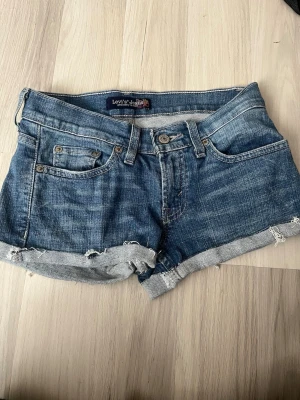 Vintage  Levi's shorts  - Säljer ett par vintage blå jeansshorts från Levi's med råa kanter och uppvikta. Perfekta för varma dagar och ger en cool, avslappnad vibe. Shortsen är riktigt lågmidjade!