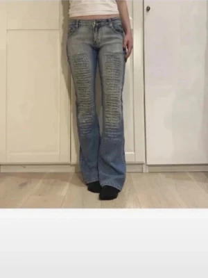 Blå bootcut jeans med slitningar - Säljer ett par ljusblå bootcut jeans med tydliga slitningar framtill och lätt tvättad look. Jeansen har klassisk femficksmodell och normal midja. Perfekta för dig som gillar retrovibbar och en avslappnad stil. Första bilderna är inte mina. Kan tyvärr inte se vilket märke de är och knappen sitter lite dåligt men fortfarande så de håller. Midjemått är 84 cm och innerbenslängden 84