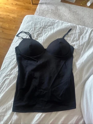 Svart body med tunna axelband - Snygg svart body med vadderade kupor och tunna justerbara axelband. Kroppsnära passform och slät yta, perfekt att styla under skjortor eller tröjor. Materialet känns mjukt och stretchigt för extra komfort. passar både Xs och S❣️❣️