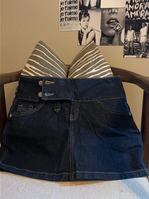 Mörkblå jeanskjol bershka - Trendig mörkblå jeanskjol med hög midja och dubbla knappar framtill. Kjolen har klassiska fickor fram och bak, samt kontrastsömmar som ger en snygg detalj. Perfekt för dig som gillar en cool och avslappnad stil.
