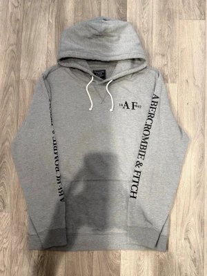 Abercrombie & Fitch Tunn Hoodie Grå Strl M - Abercrombie & Fitch grå tunn hoodie med klassisk passform som funkar till allt, storlek M, axelbredd 46 cm, bröstvidd 56,5 cm, armlängd 65 cm, midja 51 cm, längd 70,5 cm, i fint skick.