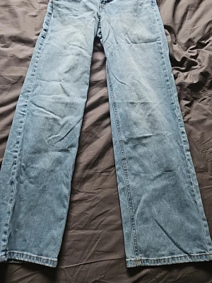 Ljusblåa jeans från KappAhl  - Säljer ett par ljusblå jeans med rak och bred passform. Jeansen har klassisk femficksdesign och är tillverkade i denim. Perfekta för en avslappnad och trendig stil.