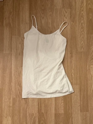 Vit enkel linnetopp med smala band - Säljer en vit linnetopp med smala axelband och rak passform. Toppen är ärmlös och har en mjuk, lätt känsla som passar perfekt till sommaren. Enkel och stilren design som är lätt att matcha med olika outfits.