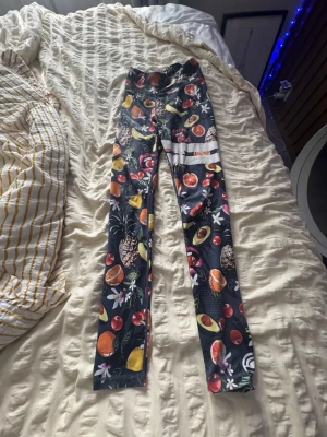 Mönstrade leggings från Stronger - Färgglada leggings från Stronger med mörkblå bas och tropiskt fruktmönster med avokado, apelsin, ananas och blommor. Hög midja och stretchigt material som sitter skönt. Perfekta för dig som vill sticka ut på gymmet eller i vardagen. Lappen där bak har tvättats bort men storlek Xs❣️