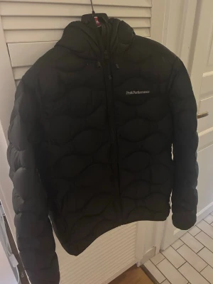 Svart dunjacka Peak Performance - Snygg svart dunjacka från Peak Performance med huva och dragkedja framtill. Nypris 3200 kr | Mitt pris 1500 kr. Väldigt bra skicka med inget slitage 