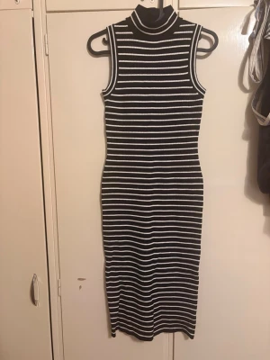 Svartvit randig ärmlös klänning från Michel kors  - Säljer en svartvit, ärmlös klänning med smala horisontella ränder och hög krage. Klänningen är figurnära och har en längre modell som passar perfekt för dig som gillar en stilren och enkel look.