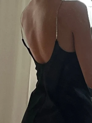 Kort klänning - Snygg svart klänning med tunna, glittriga axelband och öppen rygg. Klänningen har en rak passform och är ärmlös, perfekt för dig som vill ha en stilren och elegant look. Aldrig använd💞