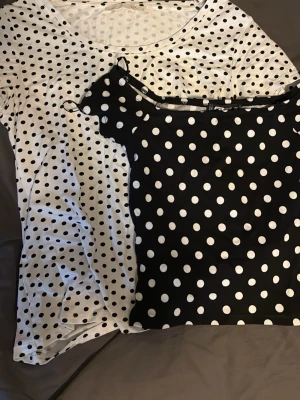 Två prickiga toppar  -  Två toppar i storlek M. Vit t-shirt med svarta prickar från Lager 157 och svart prickig majtröjan med tunna axelband från New Yorker.