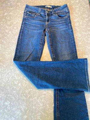 Blå jeans från Gina Tricot Low waist - Säljer ett par klassiska blå bootcut jeans från Gina Tricot i storlek 158. Jeansen har fem fickor, bälteshällor och stängs med knapp och dragkedja. Perfekta till en avslappnad look och passar till det mesta!