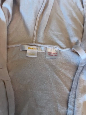 Ljusbeige/rosa hoodie från Gina Tricot - Ljusbeige/rosa hoodie från Gina Tricot med dragkedja framtill och ribbade muddar vid ärmslut och nederkant. Tillverkad i mjukt material och har en klassisk huva. Perfekt för en avslappnad och trendig look.