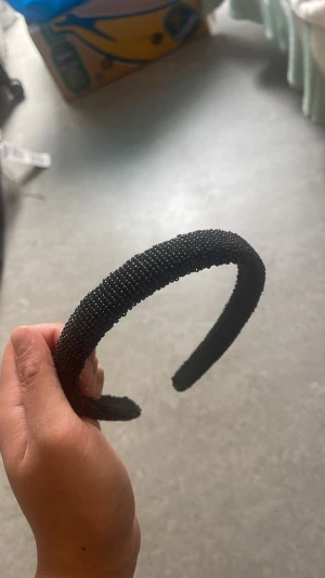 Svart pärlprydd hårband Beck Söndergaard - Snyggt svart hårband från Beck Söndergaard, täckt med små svarta pärlor som ger en lyxig och trendig känsla. Perfekt accessoar för att lyfta din look och hålla håret på plats. Hårbandet har en klassisk bågform och är bekvämt att bära.