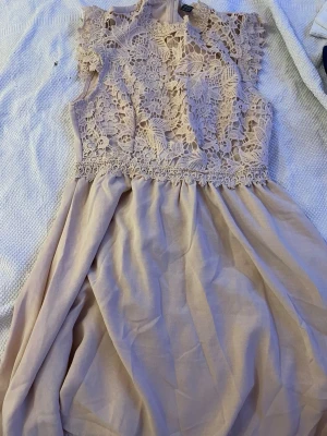 Rosa spetsklänning med volang - Söt rosa klänning med detaljerad spets upptill och volangig kjol. Klänningen är ärmlös och har en romantisk look med blommigt spetsmönster. Perfekt för sommarens alla tillfällen.