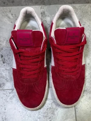 Röda sneakers från Valentino - Snygga sneakers från Valentino i rött mocka med vita detaljer och matchande röda skosnören. Yttersulan har ett unikt kamouflagemönster och märkeslogga. Skorna har en klassisk låg profil och är perfekta för dig som vill sticka ut.