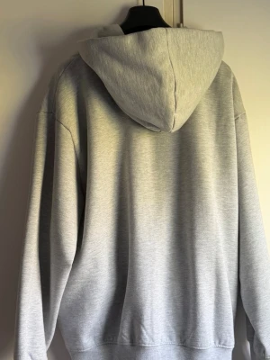 Grå hoodie från Acne Studios - Snygg grå hoodie från Acne Studios med klassisk huva och relaxed fit. Tillverkad i mjukt bomullsmaterial och har en diskret rosa etikett med logga i sidan. Perfekt för en chill och stilren look.