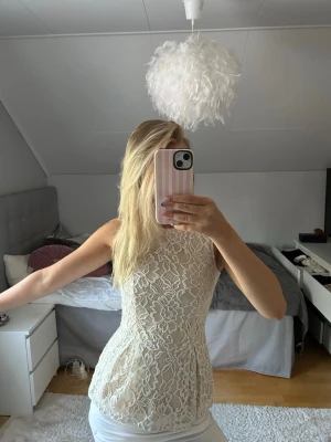 Beige spetslinne med blommönster - Säljer ett superfint beige linne i spets med blommigt mönster. Toppen är ärmlös, har rund halsringning och figurnära passform. Perfekt att styla till jeans eller kjol för en trendig look. Materialet är genombruten spets som ger en romantisk vibe. Aldrig använd