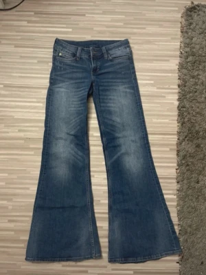 Blå utsvängda jeans med låg midja - Säljer ett par blå jeans med utsvängda ben och låg midja. Perfekta för dig som gillar retrostil och vill ha ett statement-plagg i garderoben.