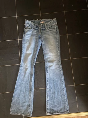 Ljusblå bootcut jeans med rå kant - Säljer ett par ljusblå helt nya bootcut jeans med fransig, rå kant i midjan. Jeansen har klassisk femficksmodell och är tillverkade i denim med lätt tvättad 