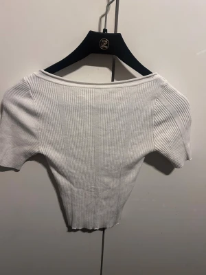 Vit ribbad croppad topp - Säljer en vit ribbad topp med korta ärmar och öppen rygg. Modellen är croppad och har en tajt passform som framhäver figuren. Perfekt att styla med höga jeans eller kjol för en trendig look.