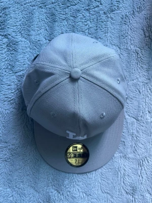 Ljusgrå LA 59FIFTY keps - Snygg ljusgrå keps från New Era med LA-logga broderad framtill i vitt. Klassisk rak skärm och strukturerad passform. Tillverkad i ett tåligt tyg som ger en clean och modern look. Perfekt för dig som gillar streetwear och sportig stil.