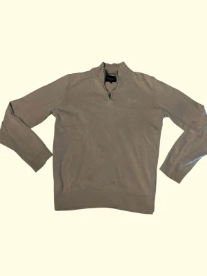 Beige tröja med halv dragkedja - Stilren beige tröja med halv dragkedja och ståkrage. Tröjan har långa ärmar och ribbade muddar vid ärmslut och nederkant. Perfekt för lager på lager och enkel att matcha med olika outfits.