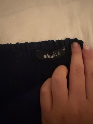 Mörkblå volangkjol från Gina Tricot - Supersöt mörkblå kortkjol från Gina Tricot med bred smock i midjan och dubbla volanglager nedtill. Kjolen har en flowy känsla och passar perfekt till både sneakers och boots. Tillverkad i ett lätt och luftigt material.