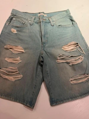 Ljusa slitna jeans jorts Levi's - Säljer ett par ljusblå jeansshorts/jorts från Levis. Aldrig använt. Skulle säga att dom är storlek 40/42 beroende på hur man vill att dom ska sitta.