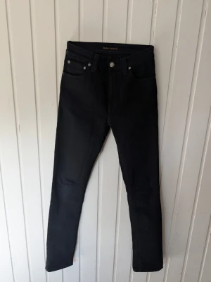 Svarta skinny jeans från Nudie Jeans - Säljer ett par svarta skinny jeans från Nudie Jeans i storlek W25 L32. Jeansen har klassisk femficksmodell, hög midja och smal passform hela vägen ner. Tillverkade i stretchigt denimtyg för extra komfort. Perfekta till en avslappnad streetstyle-look.