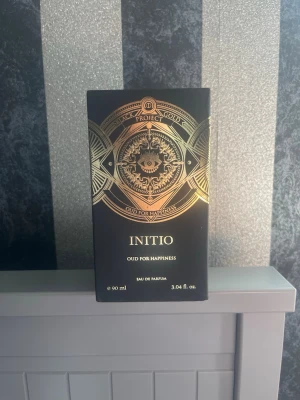 Initio Oud For Happiness parfym 90 ml - Lyxig parfym från Initio, Oud For Happiness, i en elegant svart och guld flaska med mystiskt ögonmotiv. Flaskan rymmer 90 ml Eau de Parfum och har en exklusiv design med geometriska detaljer och guldfärgade inslag. Perfekt för dig som gillar unika och djupa dofter. Ganska ny endast testsprejad.