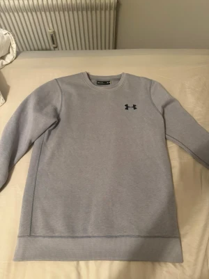 Ljusgrå sweatshirt från Under Armour - Ljusgrå sweatshirt från Under Armour med rund halsringning och diskret logga på bröstet. Tröjan har ribbade muddar vid ärmslut och nederkant samt mjuk insida i fleece. Perfekt för en avslappnad och sportig stil.