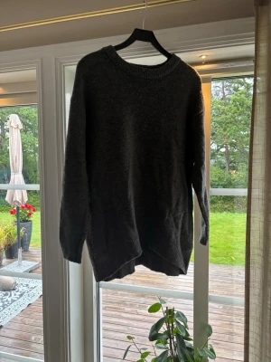 Mörkgrå oversized stickad tröja - Mysig och oversized stickad tröja i mörkgrått med rund halsringning och långa ärmar. Tröjan har ribbstickade muddar vid hals, ärmslut och nederkant. Perfekt för lager på lager och chill dagar.