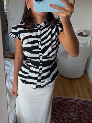 Zebra blus - Säljer en zebramönstrad blus i svart och vitt med knappar framtill och liten krage. Blusen har korta volangärmar och figurnära passform. 
