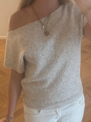 Ljusbeige off shoulder topp - Fin ljusbeige stickad topp med off shoulder-design och korta ärmar. Tillverkad i ett mjukt, stickat material. Kan användas både som offshoulder på en sida eller båda sidorna! Använd en gång.