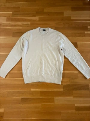 Beige stickad tröja i kashmir  - Klassisk begie stickad tröja med rund hals och långa ärmar. Tröjan har en enkel och stilren design, perfekt att matcha med jeans eller shorts. Tillverkad i kashmir.