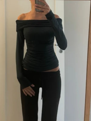 Grön offshoulder topp med rynk - Säljer en mörkgrön offshoulder topp med långa ärmar och snygga rynkdetaljer både fram och bak. Toppens passform är tight och den har en croppad stil som framhäver midjan. Perfekt för dig som vill ha en trendig och stilren look. Använd 2 gånger och nypris är 429. Väldigt stretchig så passar många stl. Jag har vanligtvis xs