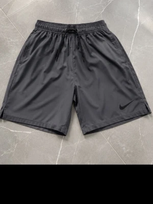 Svarta träningsshorts från Nike - Snygga svarta träningsshorts från Nike med elastisk midja och dragsko för perfekt passform. Tillverkade i ett lätt och snabbtorkande material, perfekta för gymmet eller löprundan. Diskret Nike-logga på vänster ben.
