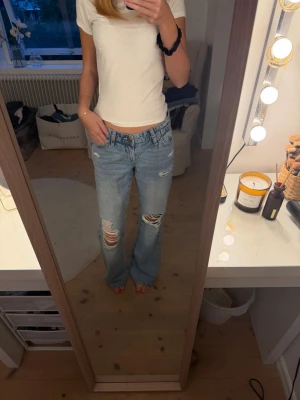Ljusblå slitna raka jeans - Säljer ett par ljusblå jeans med raka ben och slitningar på båda knäna. Jeansen har klassisk femficksmodell och låg midja. Perfekta för en avslappnad och trendig look.