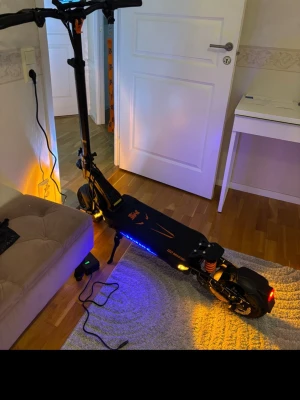 Kukirin G2 Master - Säljer en svart elscooter Kukirin G2 master med LED-belysning i blått och vitt, robusta däck och stötdämpare. Scootern har digital display på styret och orange detaljer på ramen. Perfekt för dig som vill ta dig fram snabbt och smidigt i stan. Dubbla motorer, 20.8 Ah 52v batteri, helt ny aldrig använd, 0km körd, toppfart 78km/h 2 nycklar 
