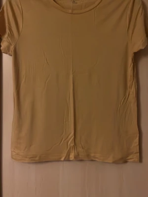 Beige t-shirt från Lindex - En basic beige t-shirt från Lindex i mjuk bomull. Klassisk rund halsringning och korta ärmar. Perfekt att matcha med jeans eller kjol för en enkel och clean look.