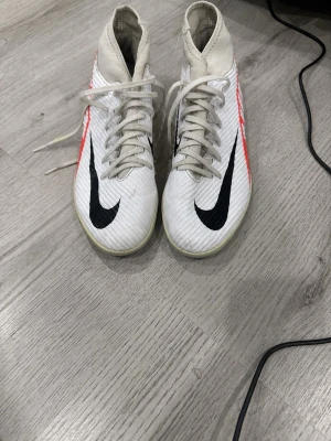 Nike Mercurial SuperFly - Säljer ett par vita Nike fotbollsskor med högt skaft och svart swoosh på ovansidan. Skorna har röda detaljer på sidorna och snörning framtill. Tillverkade i syntetmaterial för bra grepp och kontroll på planen. Pris kan diskuteras.