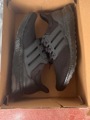 Svarta Adidas Ultraboost sneakers - Säljer ett par helsvarta Adidas Ultraboost sneakers med klassisk mesh-överdel och Boost-sula för extra komfort. Skorna har de ikoniska tre ränderna på sidan och en sportig, stilren look. Pris kan diskuteras vid snabb affär. Helt nya