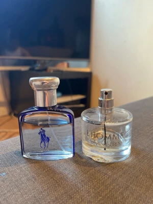 Två herrparfymer, ralph lauren  & saint laurent L'Homme - Säljer två herrparfymer: en från Ralph Lauren i en blå glasflaska med silverfärgat lock och klassisk logga, samt Yves Saint Laurent L'Homme i en rund, transparent flaska med sprayfunktion. Båda flaskorna har stilren design och passar perfekt för dig som gillar exklusiva dofter. Typ 40 ml kvar ralph lauren. Typ 10 ml kvar l’homme. kolla och bedöm skicket och mängden sjalv från bilderna. . 