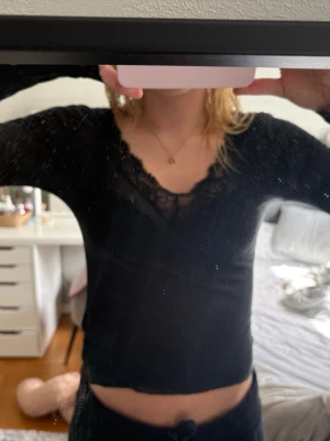 Svart långärmad topp med spets - Säljer en svart långärmad topp med v-ringning och snygga spetsdetaljer vid halsen. Toppen har en slim passform och är perfekt för dig som gillar en enkel men ändå stilren look.