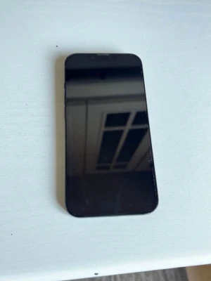 IPhone 14 nytt skick - Säljer en svart iPhone med stilren design och rundade hörn. Telefonen har två stora kameralinser på baksidan och den klassiska Apple-loggan. Skärmen är stor och täcker nästan hela framsidan. Perfekt för dig som gillar snygg och modern teknik. Inga sprickor på telefonen heller!